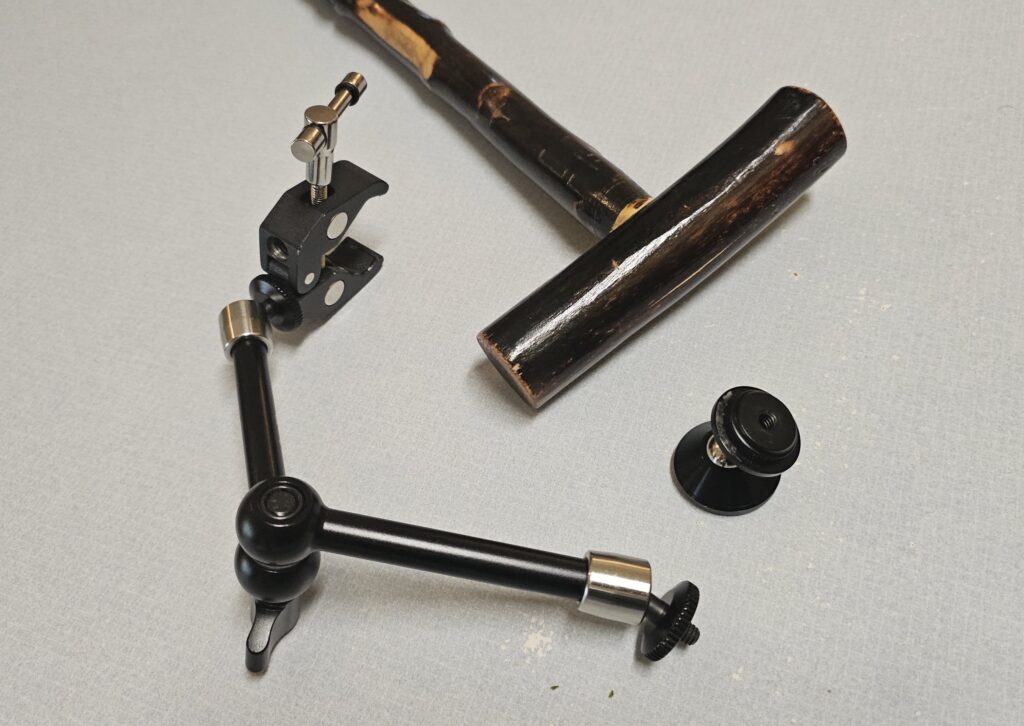 A wooden cane, a SmallRig Magic Arm with a C-Clamp, and a Coolpow  phone magnet with a thumbnut glued to one end.